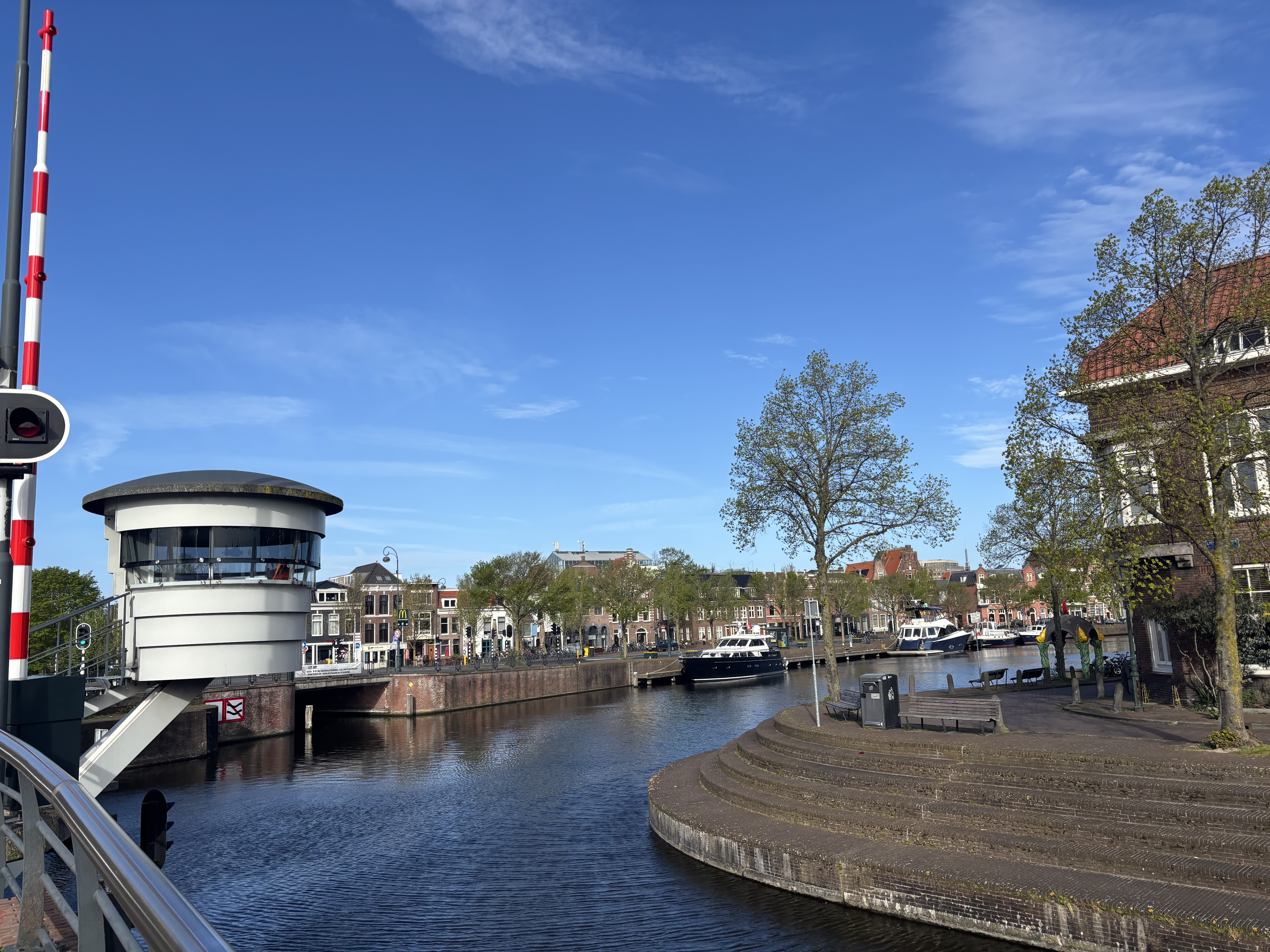 A quiet Dutch canal with a sleek modern bridge control tower on the left and pleasure boats lining the quay — historic and contemporary side by side.