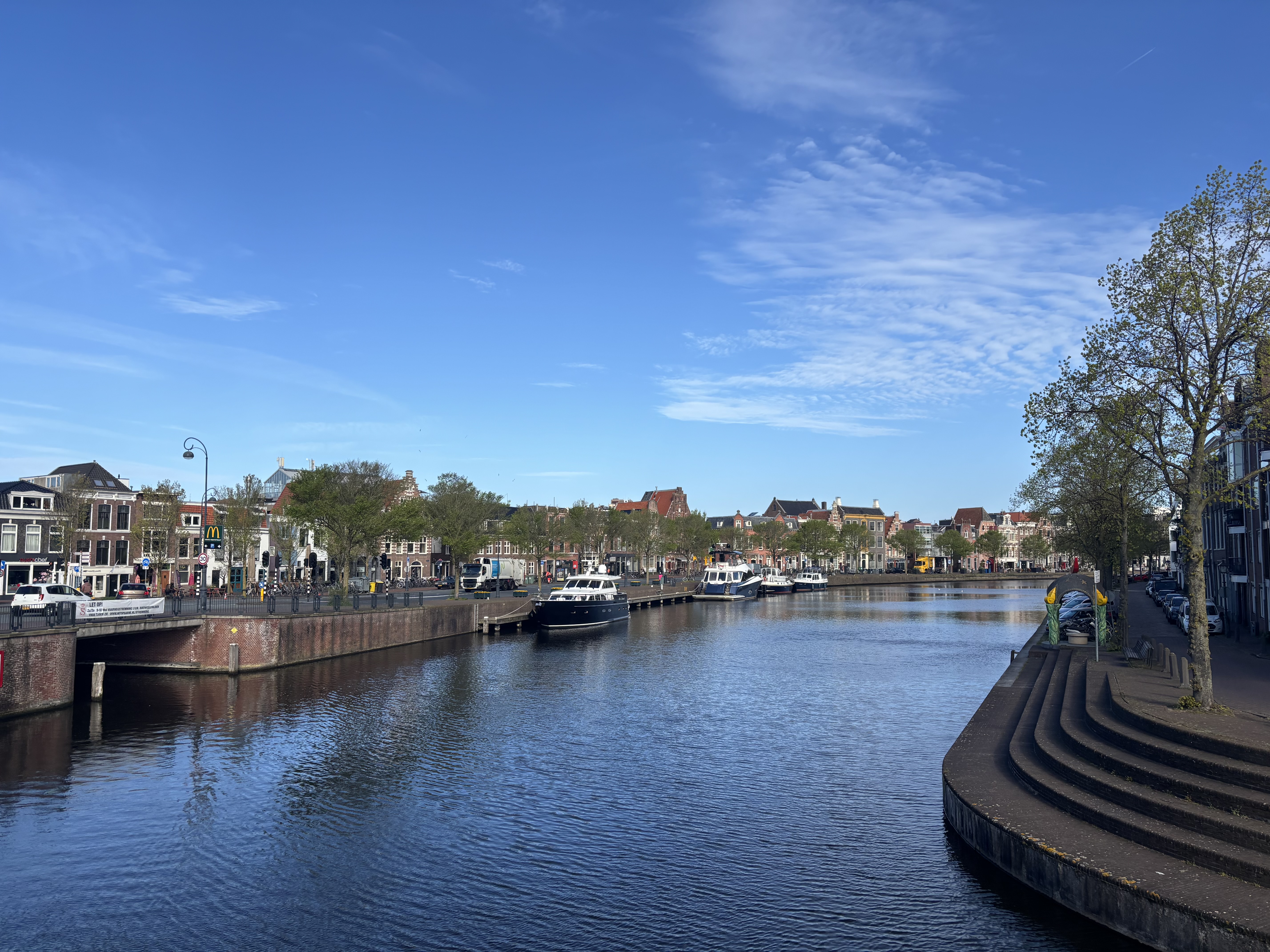 A wide harbour-canal view with houseboats, a curving brick quayside and gentle steps leading down to the water.