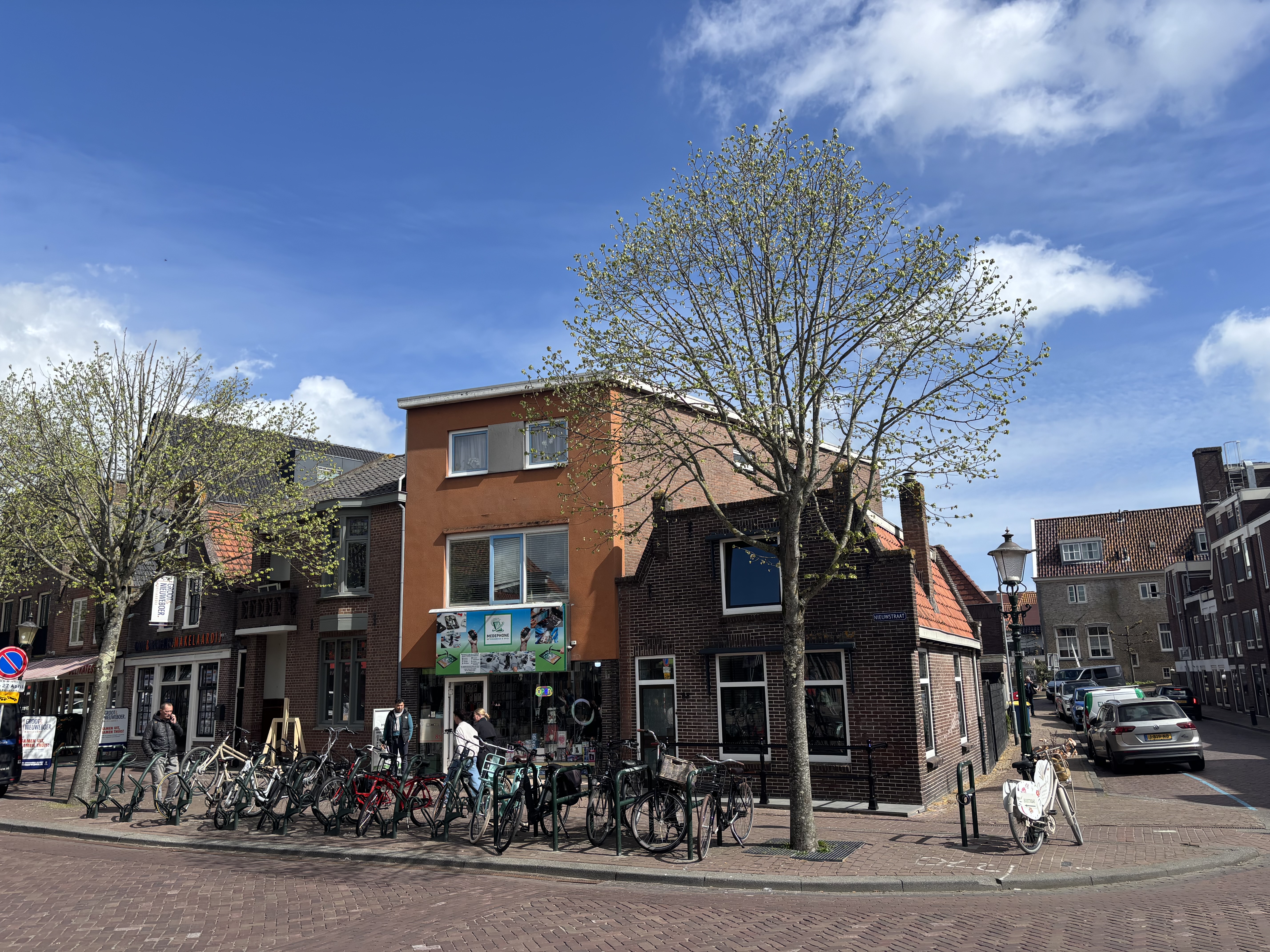 A quiet street corner in a small Dutch town — bicycles lined up against a brick shop, spring buds just opening on the tree above.