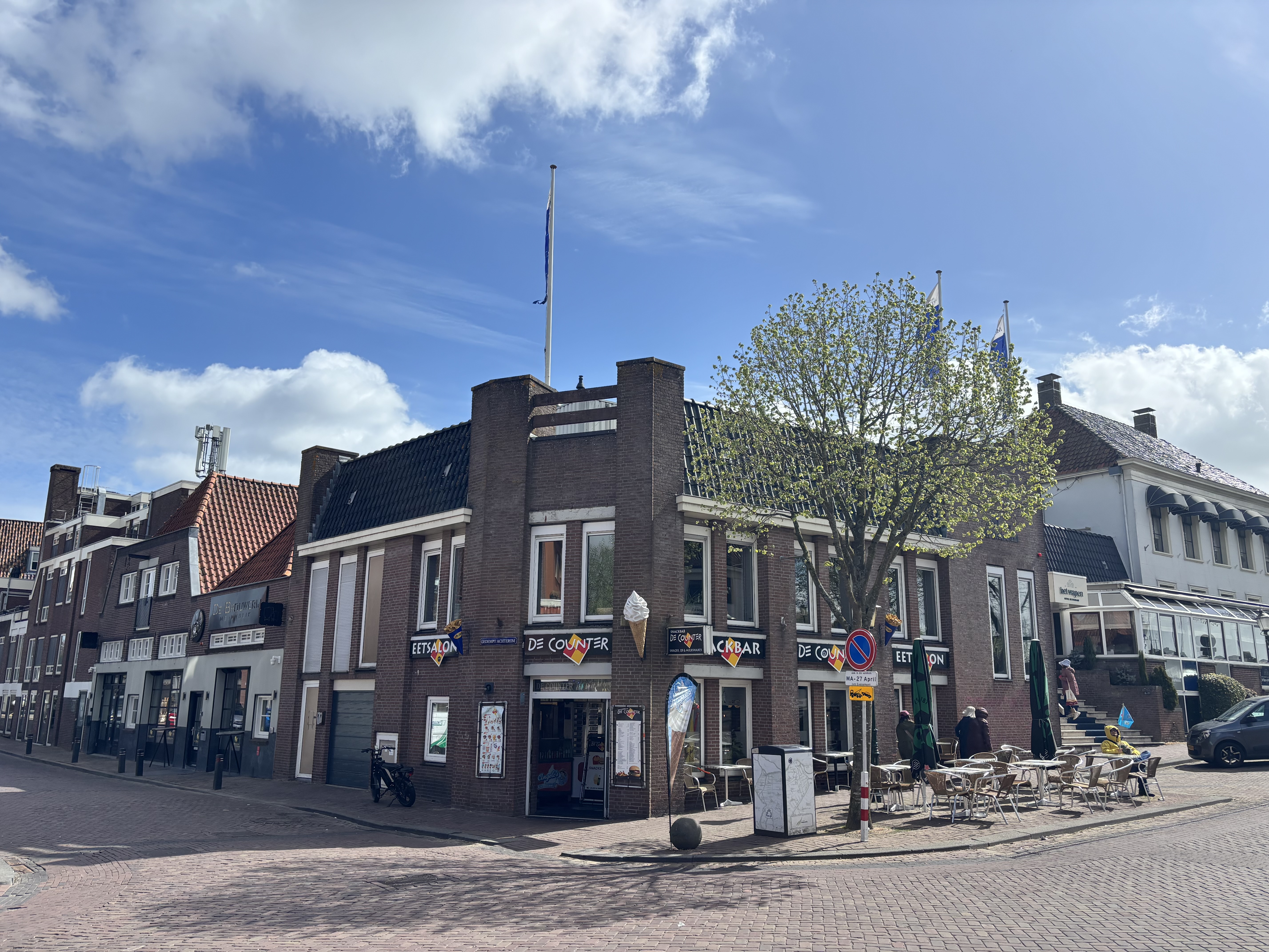 Another corner of the same town: an ice-cream parlour and café ("De Counter") with terrace seating, blue skies overhead.