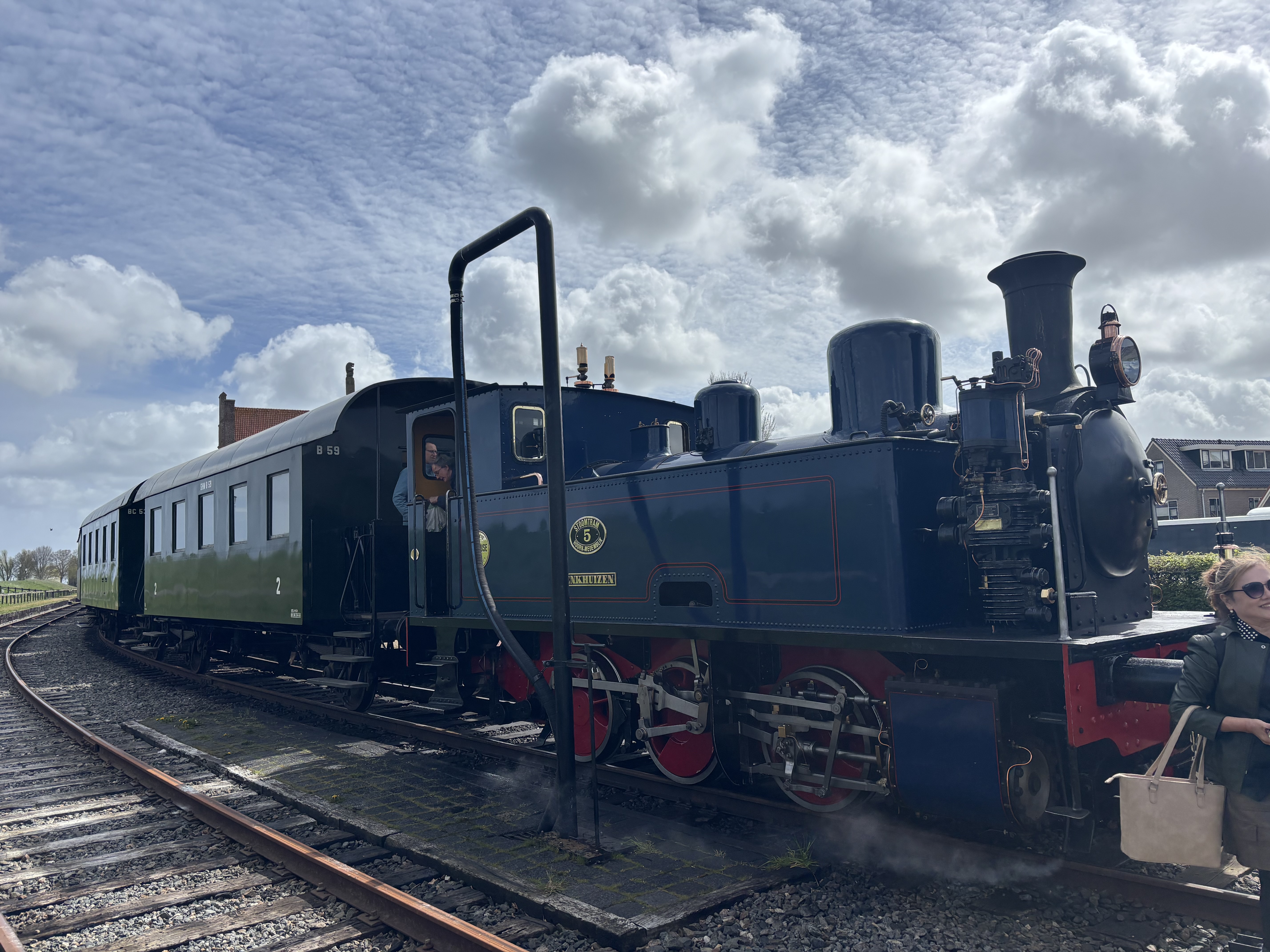 A vintage green steam locomotive paused at the platform, coupled to a wooden passenger carriage — the start of the heritage railway ride.