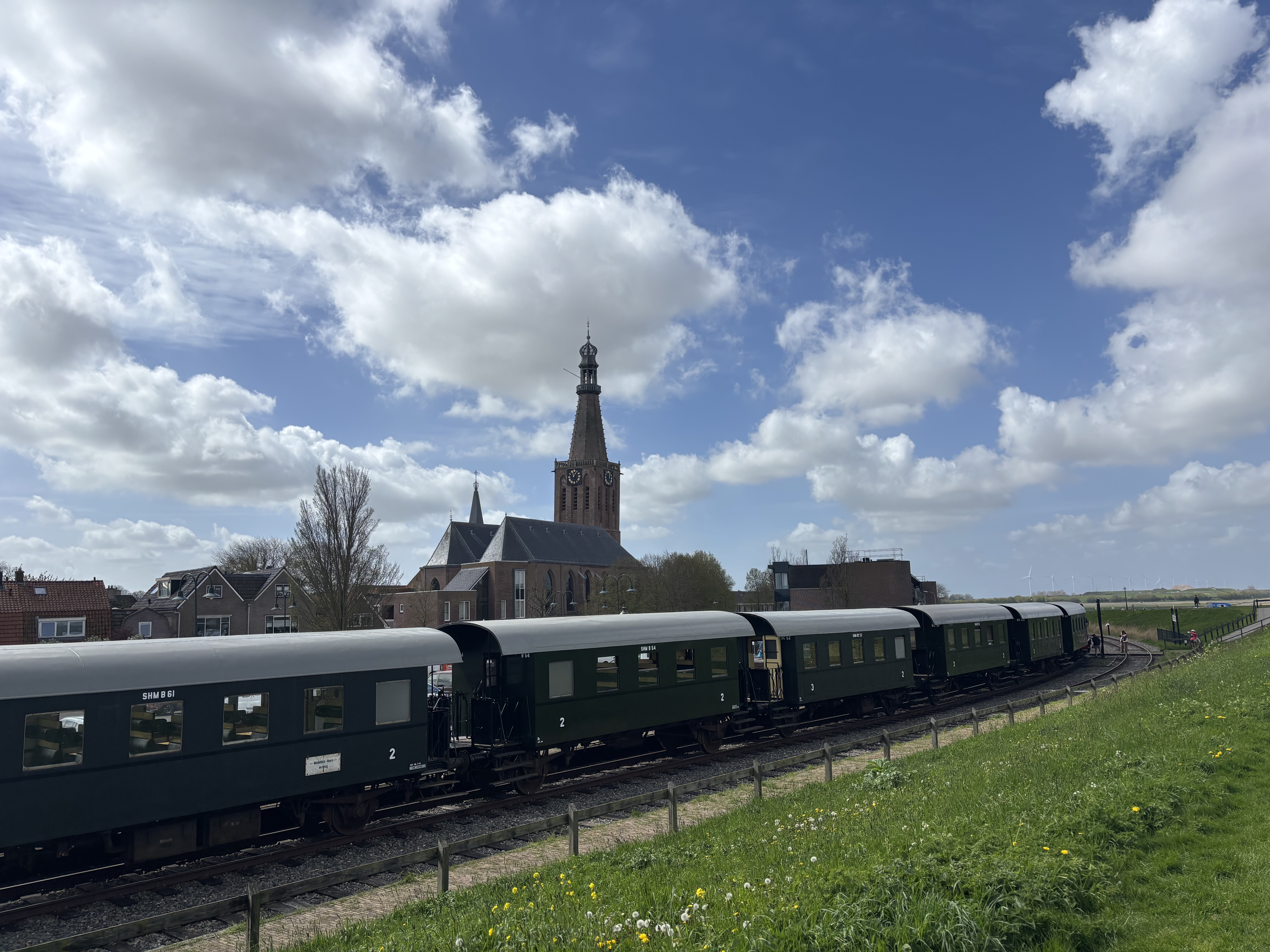 The steam train rolling past a classic Dutch village, the spire of the old church rising above red-tile rooftops.