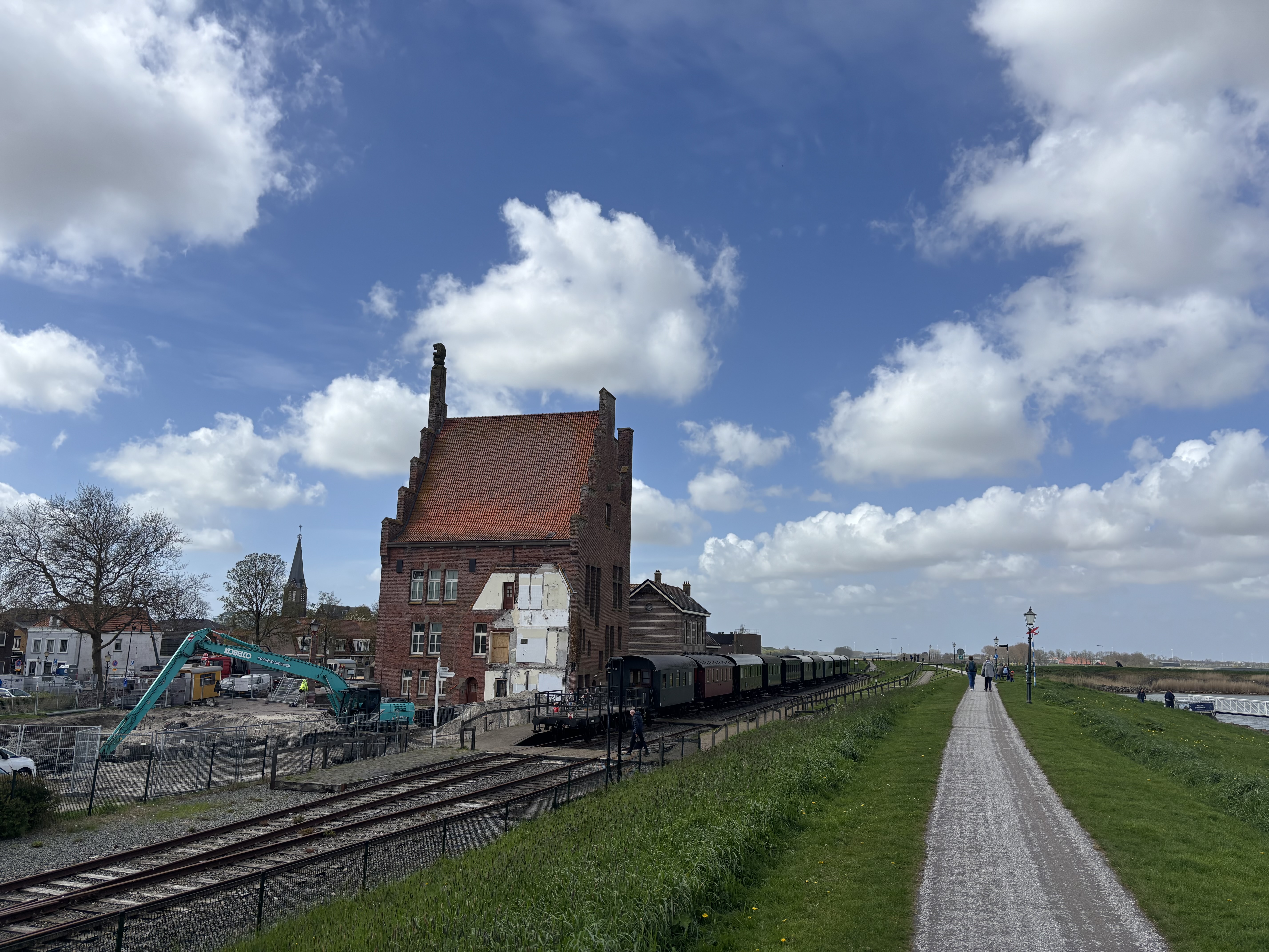 A striking stepped-gable brick warehouse beside the tracks — heritage carriages parked alongside, dyke path stretching into the distance.